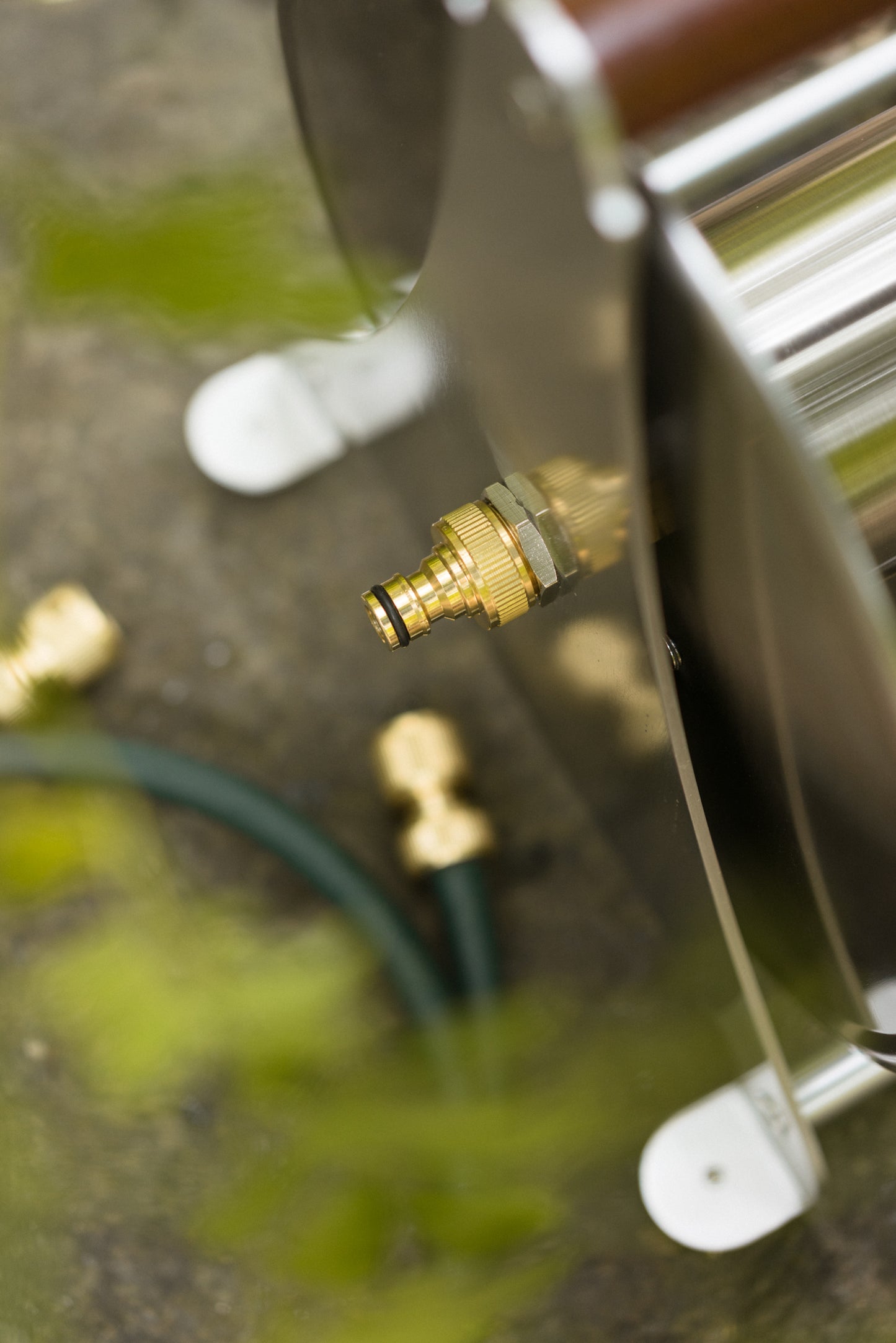 Close-up of a garden hose nozzle and connector on a reflective surface with blurred background