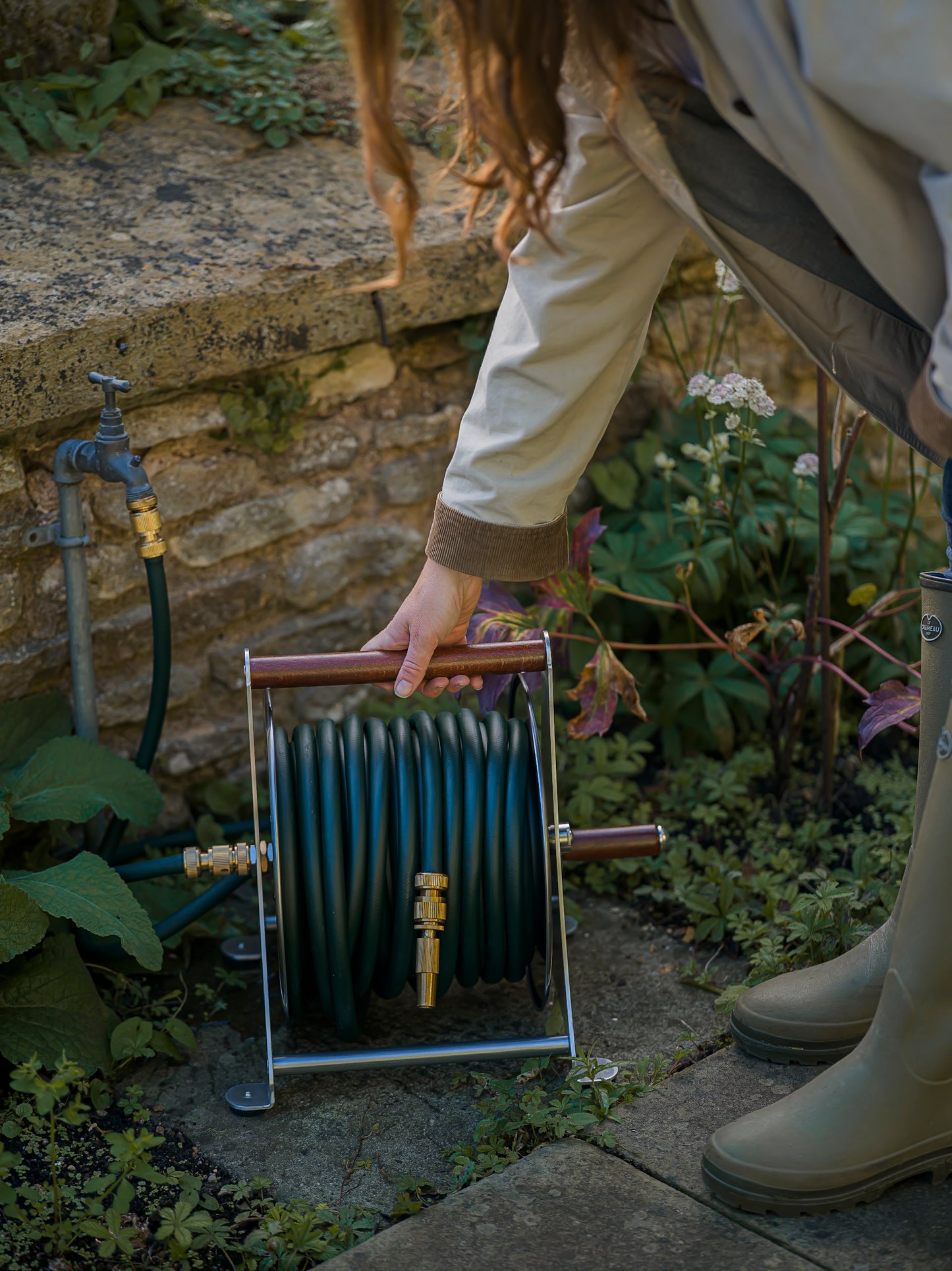 Person holding a garden hose reel in a garden setting